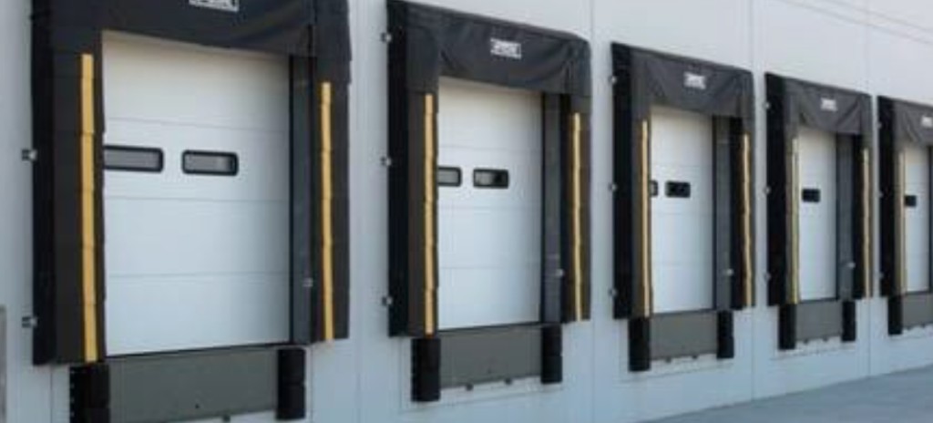 Commercial roll-up door installation at a loading bay with pallets and crew